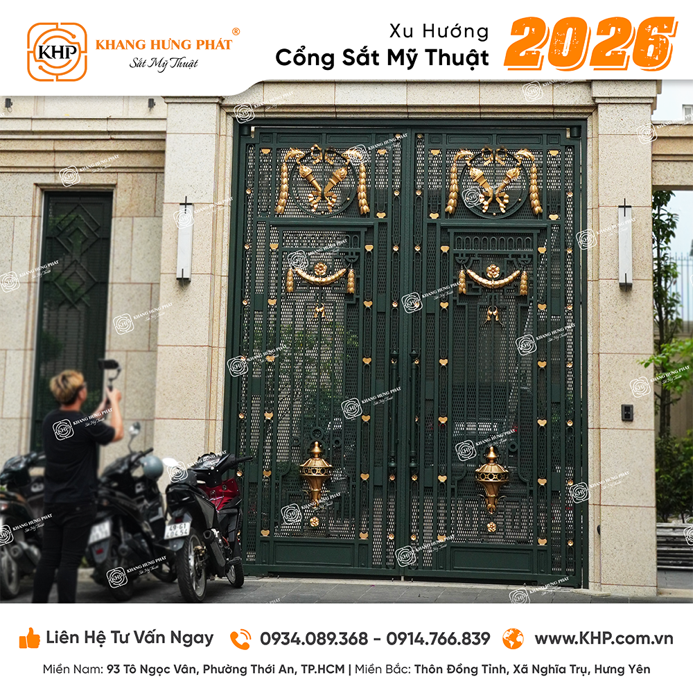 Mẫu cổng sắt tấm đột lưới ô kín (Mã số: KHP-2026-04) phủ lớp sơn xanh rêu cổ điển, điểm xuyết dải phù điêu nơ ruy băng hoàng gia rèn nổi tinh vi nhằm bảo vệ không gian riêng tư.
